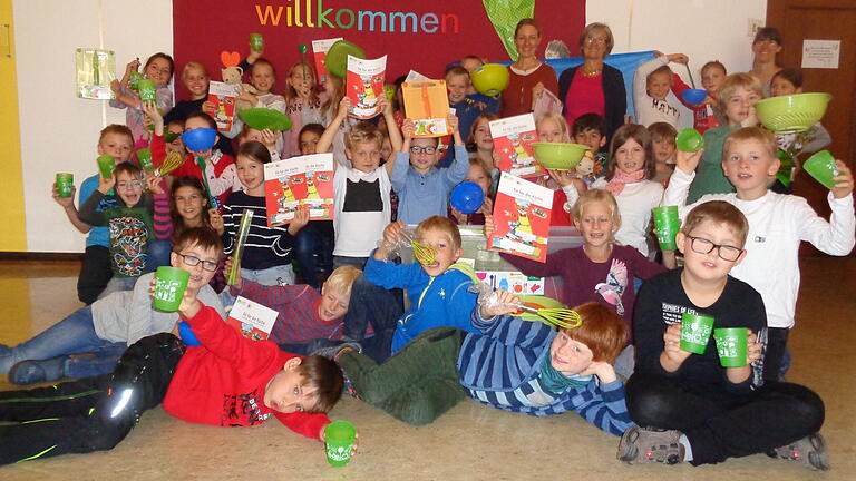 Neben Frau Ebert und Frau Löcklin und AOK-Ernährungsberaterin Ulrike Jaques freuen sich die Kinder der Klassen 3a und 3b der Goethe-Kepler-Grundschule über die Kochbox der AOK.