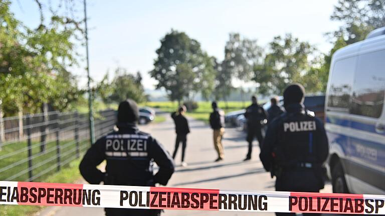 Razzien gegen völkische Siedler.jpeg       -  Einsatzkräfte der Polizei stehen hinter einer Polizeiabsperrung nach einer Razzia in Hesselbronn.