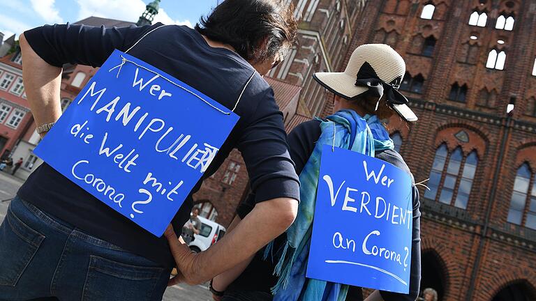 Auf einer Demonstration gegen die Maßnahmen zur Eindämmung der Corona-Pandemie tragen zwei Frauen Schilder mit den Aufschriften: 'Wer manipuliert die Welt mit Corona?' und 'Wer verdient an Corona?