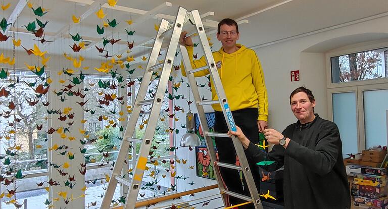 Der Initiator des großen Kranich-Mobiles Thomas Schenkel (li.) und der erfahrene Origami-Bastler Manfred Landauer hängen die letzten der 1200 Kraniche in der Giebelstadter Bücherei auf.