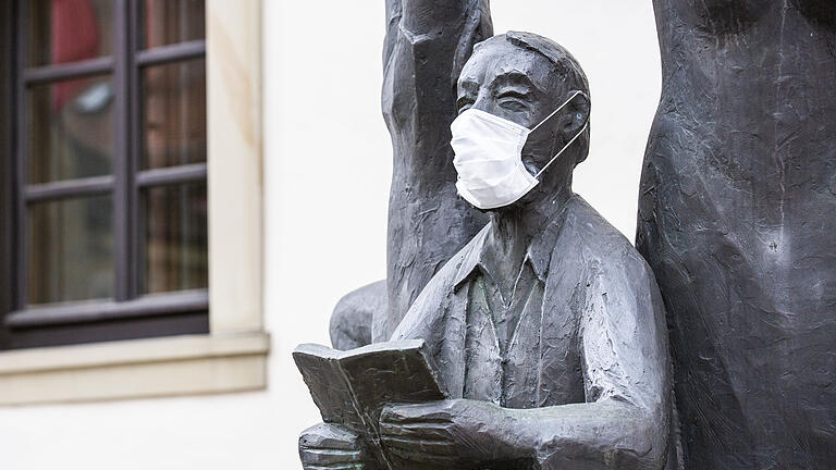 Die männliche Skulptur vom Kulturbrunnen des Künstlers Theophil Steinbrenner vor der Stadthalle in Haßfurt trägt eine Mundschutzmaske gegen eine Corona-Ansteckung.