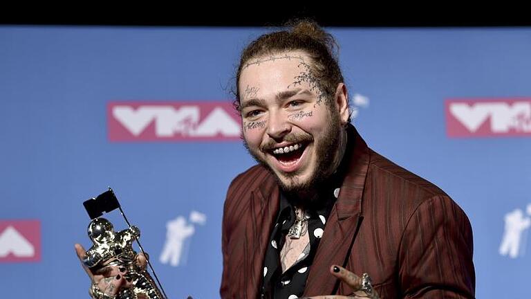 Ein Bierchen und ein Astronaut für Post Malone. Foto: an Agostini/Invision/AP       -  US-Rapper Post Malone zeigt gerne, was er hat. Mit seinem 'Diamanten-Lächeln' präsentiert er die Trophäe, die er bei den MTV Video Music Awards 2018 abräumte.