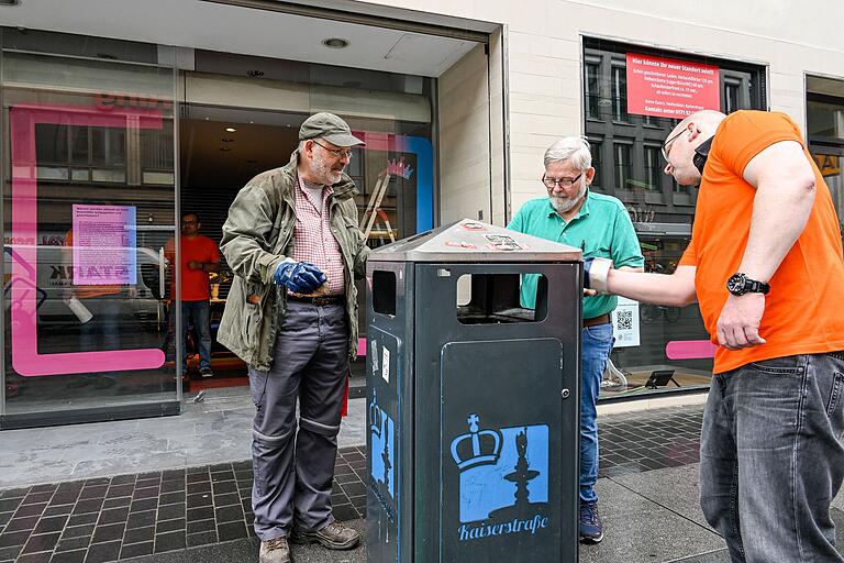 Die Hauseigentümer Joachim Drescher und Franz Wohlfart und Architekt Lars Winkler kratzen Aufkleber vom Mülleimer. Im Hintergrund ein neu beklebtes Schaufenster.