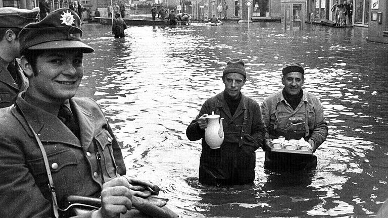 Hochwasser       -  Dramatisch &ndash; und trotz allem ein Lächeln auf den Lippen: Mit Kaffee und Kuchen geht es beim Würzburger Hochwasser im Oktober 1970 durch die Fluten. Wer erinnert sich noch daran?