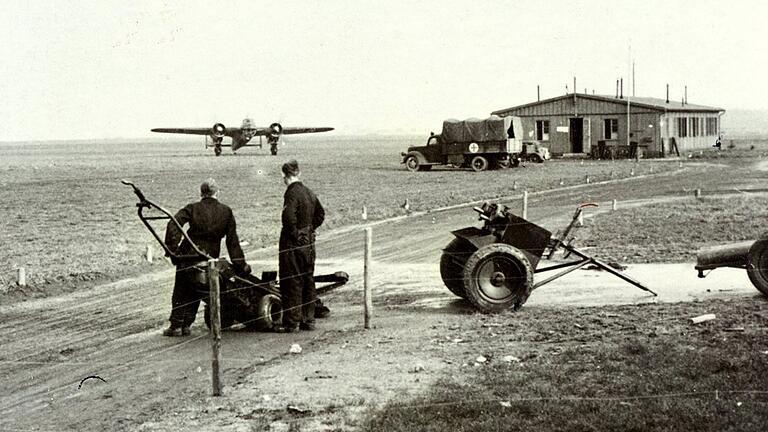 Junkers Ju 52-Flugzeuge nutzten im Zweiten Weltkrieg regelmäßig den Feldflugplatz bei Herlheim, um von hier das Afrikakorps mit Nachschub zu versorgen. Im Bild rollt ein zweimotoriger Bomber am Herleshof aus, um mit neuen Bomben beladen zu werden. Im Hintergrund ist die Baracke der Flugsicherung zu sehen. Der Rotkreuz-Lkw steht in Bereitschaft.