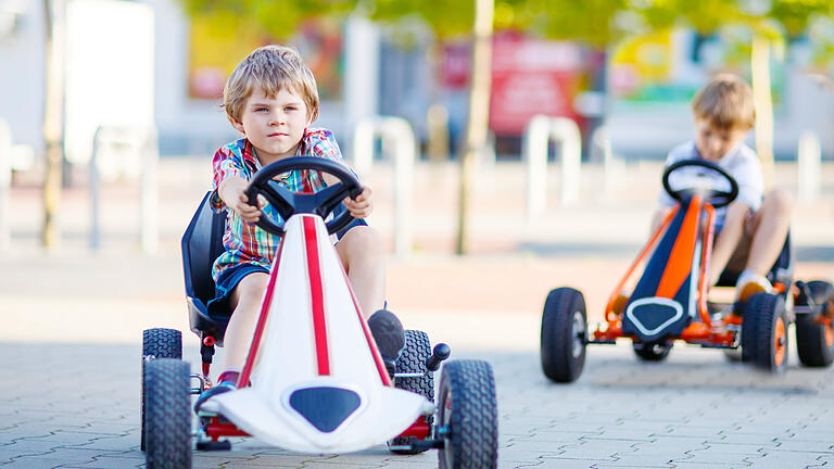 Two active little kid boys driving pedal race car in summer garden, outdoors.       -  Two active little kid boys driving pedal race car in summer garden, outdoors. Children, best friends racing with fast speed and having fun. Twins making competition