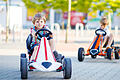 Two active little kid boys driving pedal race car in summer garden, outdoors.       -  Two active little kid boys driving pedal race car in summer garden, outdoors. Children, best friends racing with fast speed and having fun. Twins making competition