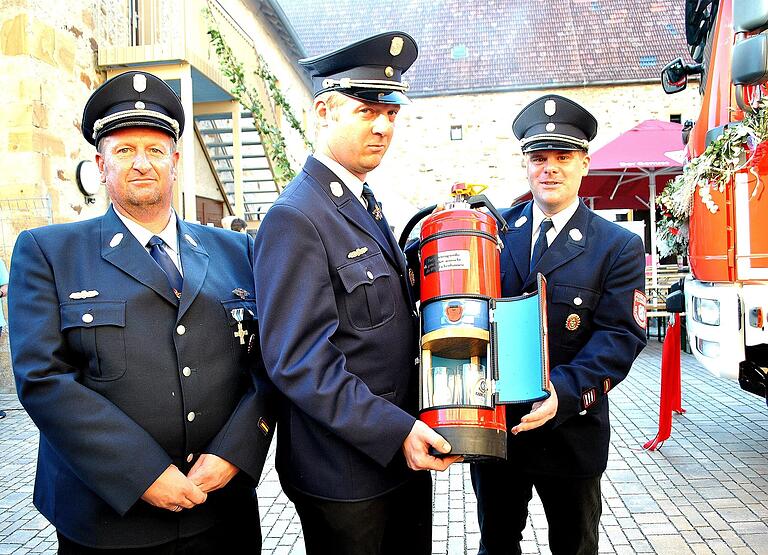 Zum Durstlöschen: Ein Geschenk der Eichenhäuser Feuerwehr an Thomas Möltner (Mitte) von Thorsten Hüllmantel (links) und Thomas Bach.