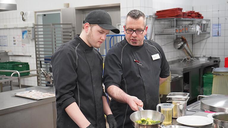 Küchenchef Sebastian Gröschl zeigt einem Auszubildenden, worauf bei der Zubereitung von Brokkoli zu achten ist. Brokkoli ist eine Gemüsesorte, die für den Heimatteller nur bedingt geeignet ist, da das Gemüse vor allem in Italien angebaut wird.       -  Küchenchef Sebastian Gröschl zeigt einem Auszubildenden, worauf bei der Zubereitung von Brokkoli zu achten ist. Brokkoli ist eine Gemüsesorte, die für den Heimatteller nur bedingt geeignet ist, da das Gemüse vor allem in Italien angebaut wird.