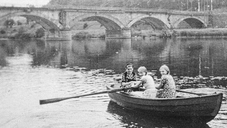 Drei junge Frauen in einem Boot. Im Hintergrund ist die Mainbrücke zu sehen. Deutlich erkennbar ist, dass zwei Bögen noch nicht ausgemauert sind.