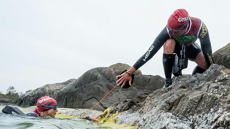 Sascha Bergerhausen (rechts) zieht Christine Karl bei der Swimrun-Weltmeisterschaft 2023 aus dem Wasser. Die beiden Ochsenfurter haben an einem der härtesten Ausdauerrennen teilgenommen.