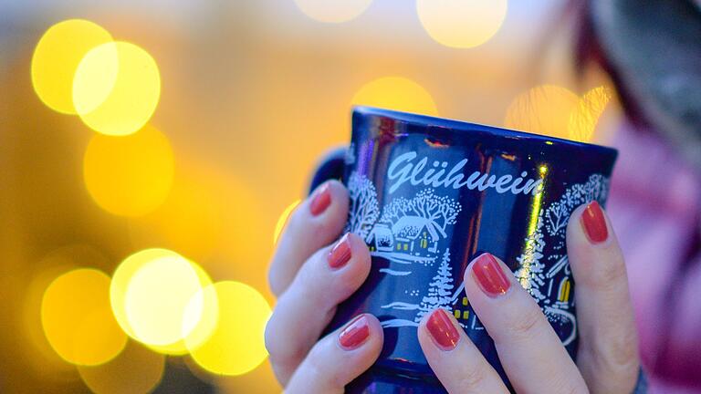 Frau hält Tasse mit Glühwein in den Händen       -  Nichts wärmt besser auf dem Weihnachtsmarkt als ein heißer Glühwein.