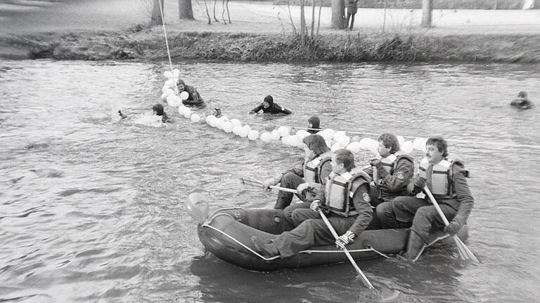 Advent-Saaleschwimmen  der Wasserwacht Bad Kissingen       -  Zum 10. Jubiläum 1984 konnte sich die Schwimmer Lose aus den Luftballons ergattern, die an einer Leine über der Saale hingen.