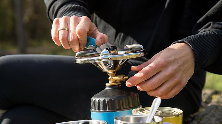 Ein Campingkocher wird auf den Einsatz vorbereitet       -  Sicher kochen unterwegs: Wer sich auf Reisen das Essen mit einem Campingkocher zubereitet, sollte vor jedem Einsatz darauf achten, dass alle Bauteile unbeschädigt sind.