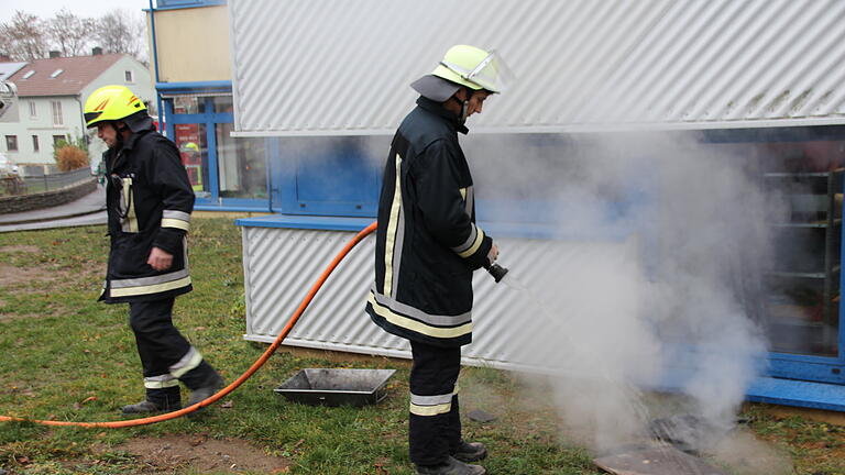 Feuerwehrleute löschen qualmende Holzteile ab, die Kameraden aus dem Fenster des Brennofenraums der Mittelschule Gerolzhofen geworfen hatten.