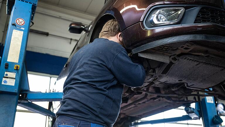 Kfz-Werkstatt       -  Ein Mechaniker schaut in einer Kfz-Werkstatt in den Radkasten eines Autos.