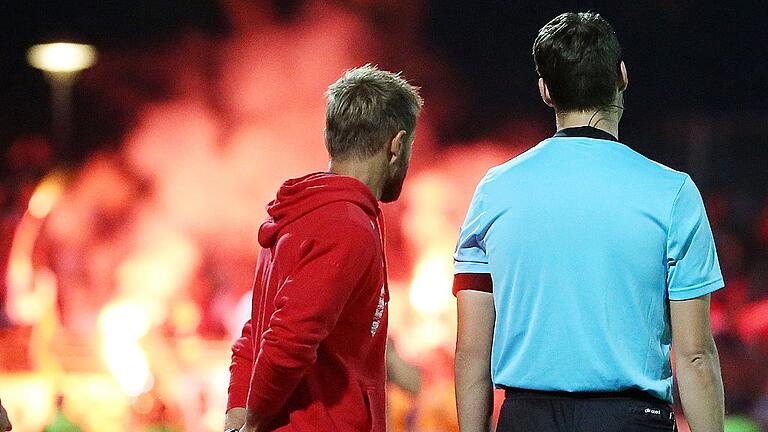 Fussball, BFV Verbandspokal, Achtelfinale, 1. FC Schweinfurt 05 - FC Würzburger Kickers       -  Hilflose Beobachter: Kickers-Trainer Michael Schiele und Schiedsrichter-Assistent Christopher Schwarzmann sehen, wie im Würzburger Fanblock zum wiederholten Mal gezündelt wird.