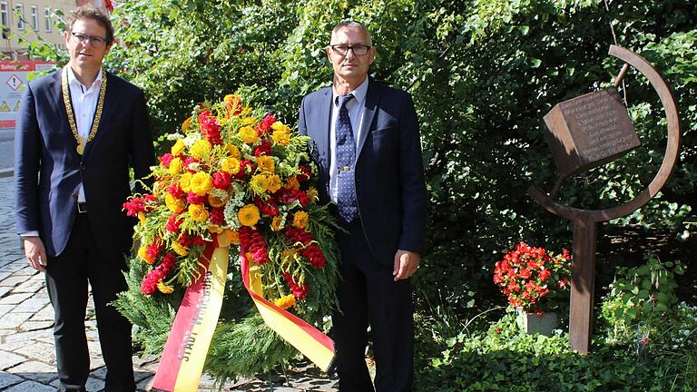 Bürgermeister Martin Heilig (links) und Roberto Paskowski (rechts), der stellvertretende bayerische Landesvorsitzende des Verbandes Deutscher Sinti und Roma, legen am Mahnmal am Paradeplatz Kränze nieder.