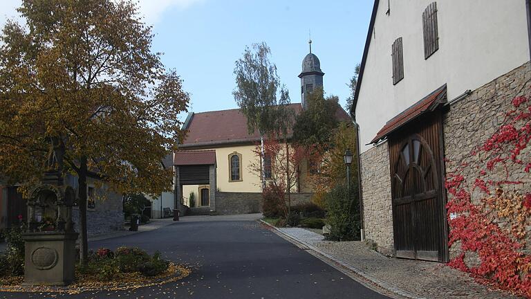 Der Dorfplatz von Binsbach&nbsp;mit Blick auf die St. Jakobus-Kirche sowie dem Bildstock und Prozessionsaltar links, der vom heiligen Georg, dem Drachentöter, bekrönt wird.&nbsp;