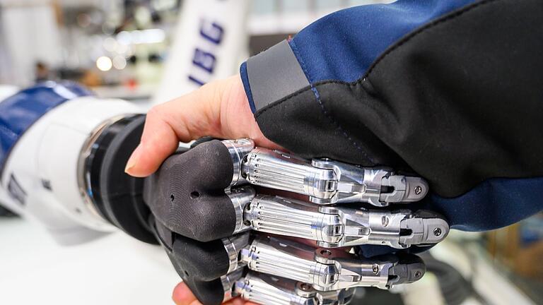 Künstliche Intelligenz Roboterhand menschliche Hand       -  An einem Stand auf einer Messe gibt ein Mann einem Roboter die Hand.