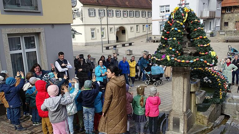 Vorschulkinder des AWO Kindergartens mit Bürgermeister Alexander Knahn sowie Vorsitzende Magdalena Roßbach und Helferinnen am geschmückten Brunnen am Höchberger Marktplatz.