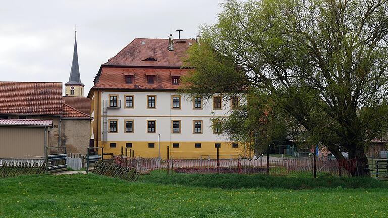 Die Rückseite des Rathauses in Prosselsheim mit einem Teil der Schlosswiese im Vordergrund und der Brücke mit ihrem Geländer über den Dettelbach (links). Hinter der 'Amtskellerei' soll einer der Eingänge zum neuen Naherholungsgebiet sein.