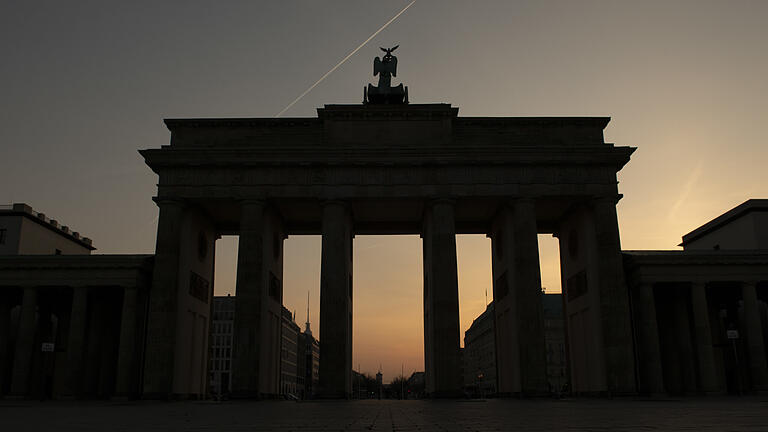 Wetter in Berlin       -  Nur als Silhouette ist das Brandenburger Tor im Gegenlicht der aufgehenden Sonne zu sehen, während ein Flugzeug über das Berliner Wahrzeichen fliegt.