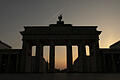 Wetter in Berlin       -  Nur als Silhouette ist das Brandenburger Tor im Gegenlicht der aufgehenden Sonne zu sehen, während ein Flugzeug über das Berliner Wahrzeichen fliegt.