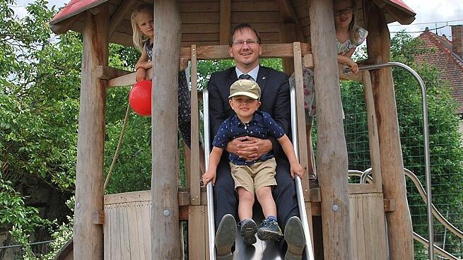 Bürgermeister Wolfram Thein beim Ausprobieren der neuen Rutsche mit seinem Sohn Willi. Josefine und Klara schauen zu.