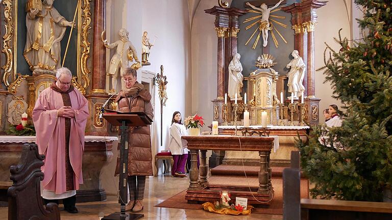 Pfarrer Helmut Rügamer und Lektorin Gabriele Meinberger in der adventlich dekorierten Pfarrkirche St. Wolfgang und mit dem Friedenslicht aus Bethlehem vor dem Altar.