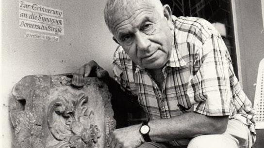 Der in Würzburg geborene deutsch-jüdische Dichter Jehuda Amichai bei einem Besuch in Würzburg 1992 – fotogfrafiert neben dem letzten erhaltenen Stein der zerstörten Hauptsynagoge.