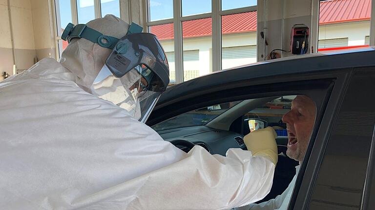 Dr. Ralph Brath nimmt fürs Foto bei Matthias Kleinhenz einen Abstrich vor. Zur Schutzkleidung gehören Overall, FFP2-Maske, Gesichtsvisier und drei übereinandergetragene Handschuhe.: Lena Pfister       -  Dr. Ralph Brath nimmt fürs Foto bei Matthias Kleinhenz einen Abstrich vor. Zur Schutzkleidung gehören Overall, FFP2-Maske, Gesichtsvisier und drei übereinandergetragene Handschuhe.: Lena Pfister