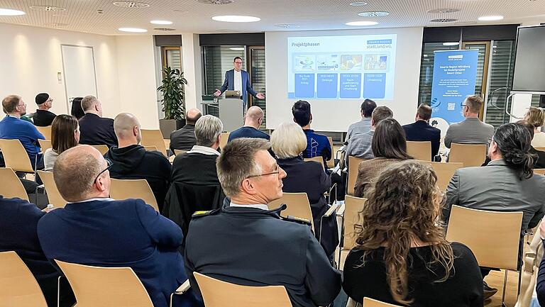 Klaus Walther (Stadt Würzburg, stehend) erklärt Stadträten, Kreistagsmitgliedern und Verwaltungsangestellten die Projektphasen der Smarten Region. Klaus Walther (Stadt Würzburg, stehend) erklärt Stadträten, Kreistagsmitgliedern und Verwaltungsangestellten die Projektphasen der Smarten Region.