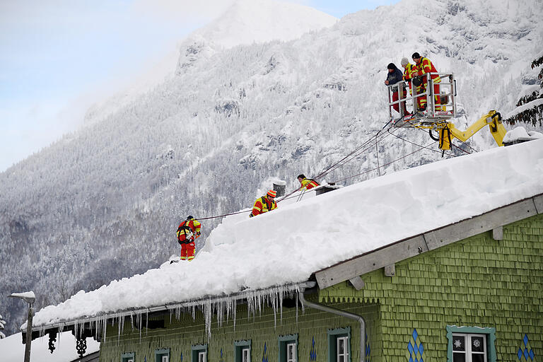 Feuerwehrleute im oberbayerischen Inzell räumen den Schnee vom Dach eines Hauses.