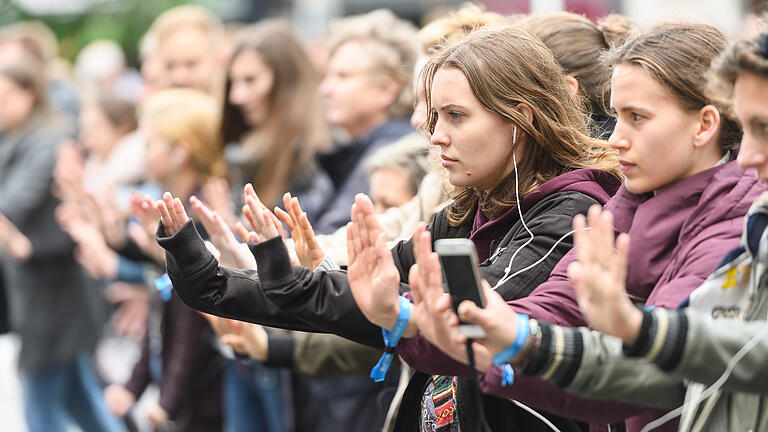 Daniel Peter       -  Um die 50 Menschen führen am Samstag (11.05.19) am Domplatz in Würzburg ein ihnen unbekanntes Theaterstück auf. Instruktionen bekommen die Laiendarsteller über Kopfhörer, die Aktion ist von UNICEF initiiert und läuft unter dem Namen &quot;Theater der 10.000&quot; zeitgleich an rund 100 Orten in Deutschland. UNICEF möchte mit der Aktion ein Zeichen für eine bessere Zukunft setzen.