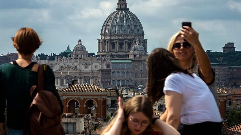 Touristen fotografieren die Kuppel des Petersdomes in Rom. Im Vatikan gibt es einen Finanzskandal.&nbsp;&nbsp;