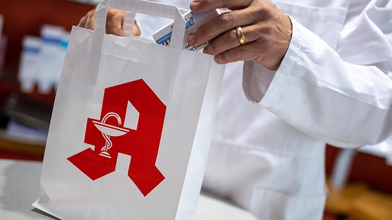 Ein Apotheker legt eine Packung mit Tabletten in eine Papiertasche mit Apotheken-Logo (Symbolfoto). Ein Apotheker legt eine Packung mit Tabletten in eine Papiertasche mit Apotheken-Logo (Symbolfoto).
