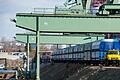 Das Zwei-Wege-Fahrzeugs ist im Hafen als Rangierlock auf den Schienen, auf Pflaster und Asphalt unterwegs und kann Waggons mit einem Gesamtgewicht von bis zu 6000 Tonnen ziehen. Über ihm sind die Stützen der Doppelwippkräne zu sehen.