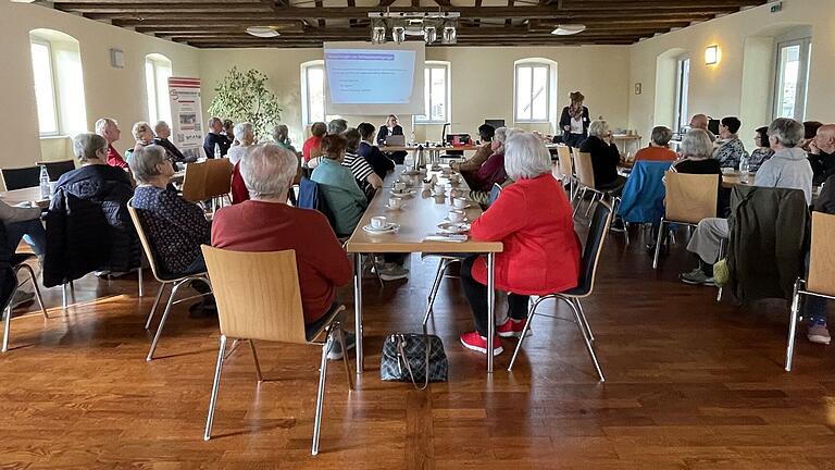 Besucherinnen und Besucher der Veranstaltung hören den Fachkräften vom Blindeninstitut Würzburg, Sabine Kampmann und Claudia Jüngling, aufmerksam zu.