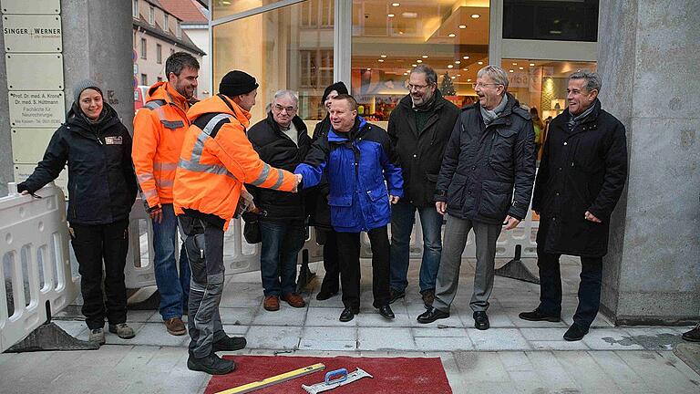 Shake Hands nach dem letzten verlegten Pflasterstein: Projektleiter Holger Döllein gratuliert dazu Polier Alfred Müller. Im Bild (von links) Ausgrabungsleiterin Judith Ehrmann, Bauleiter Matthias Knoblauch, Polier Müller, Paul Löhlein und (verdeckt) Daniela Binder von den &bdquo;Eichhörnchen&ldquo;, Projektleiter Döllein,  &bdquo;Eichhörnchen&ldquo;- Sprecher Joachim Drescher, Stadtbaurat Christian Baumgart und Planungsingenieur Heinz Zettl.