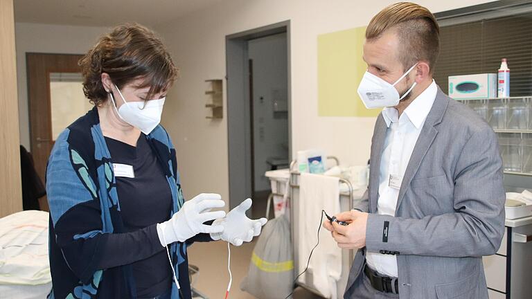 Die stellvertretende Schulleiterin Martina Weymann testet spezielle Handschuhe. Schwache Stromimpulse sorgen für Nervenirritationen, die dem Tremor bei Parkinson ähneln. Neben ihr steht Eric Pehrson, Leiter der Praxis-Ausbildung.