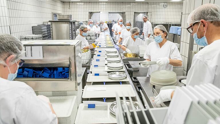 Das Portionierband läuft an. Die Mitarbeiter reihen sich rechts und links ein und befüllen die Tabletts.