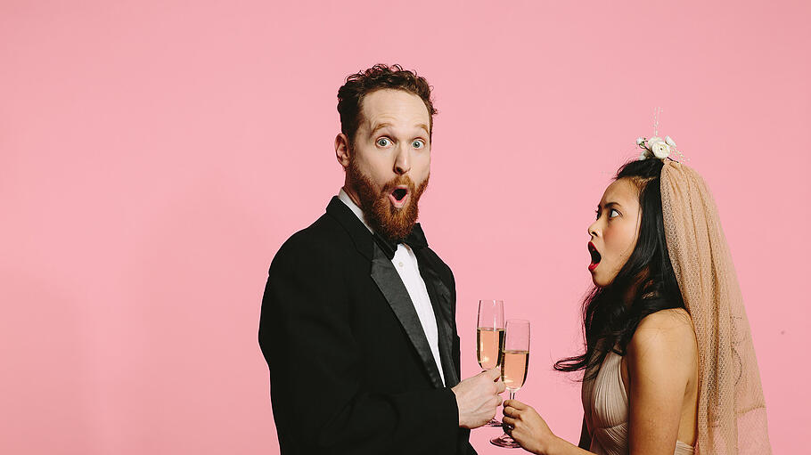 A bride and groom in shock       -  Portrait of a bride and groom cheering with champagne glasses, with expression of shock on their faces, isolated on pink