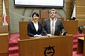 Bürgermeisterin Naomi Koshi und Bürgermeister Adolf Bauer am Rednerpult des Sitzungssaals mit Stadtwappen im Rathaus der Stadt Otsu.