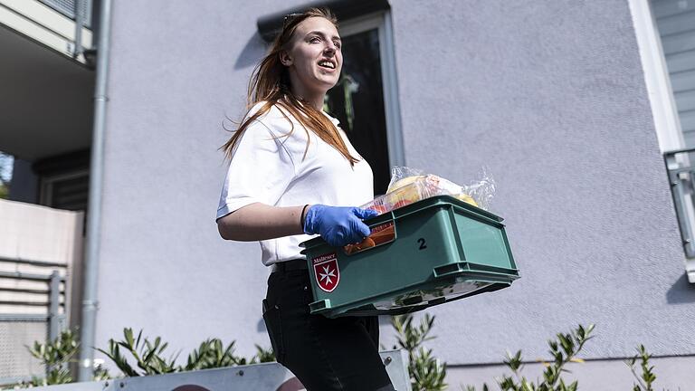 Julia Gerst vom Malteser Hilfsdienst in Freiburg trägt Lebensmittel in einer Kiste zu einem Haus. Auch in Lauda-Königshofen bieten die Malteser einen Einkaufs- und Besorgungsservice an.