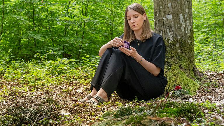 Betroffene und Mutmacherin zugleich: Anna-Lena Bolz an der Begräbnisstätte ihrer zwei Sternenkinder auf dem Waldfriedhof in Fuchsstadt. Sie betrachtet eine gehäkelte Blume, die sie als Erinnerungsstück im Krankenhaus erhalten hat. Die andere Blume befindet sich im Grab eines ihrer Sternenkinder.