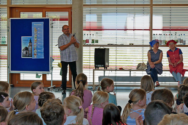 Applaus von Pfarrer Joachim Bayer. Das Pisameter neben dem Kirchturm-Plakat beweist, dass das Projektziel eines höheren Bücherturms erreicht worden ist. Rettl und Bawett (Irma Grümpel und Jutta Melzer vom Verein Kürnacher Geschicht(n), hinten von rechts) waren ebenfalls begeistert von den eifrigen Leserinnen und Lesern im Grundschulalter.