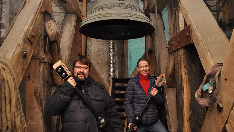 Pfarrer Oliver Störr und Barbara von Brunn mit den neuen Klöppeln für die Glocken&nbsp;der Stadtpfarrkirche St. Peter und Paul in Grünsfeld. Die beiden stehen unter einer der historischen Glocken von 1862.