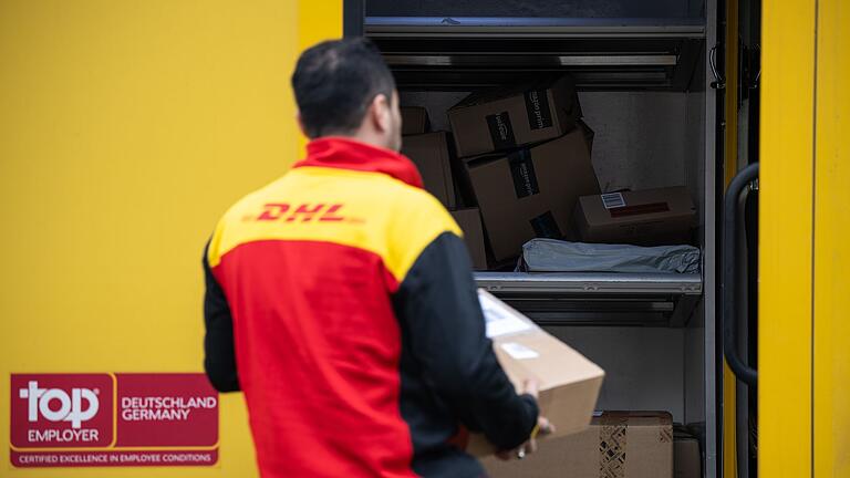 DHL-Lieferdienst       -  Ein Post-Mitarbeiter trägt ein Paket in einen Lieferwagen.