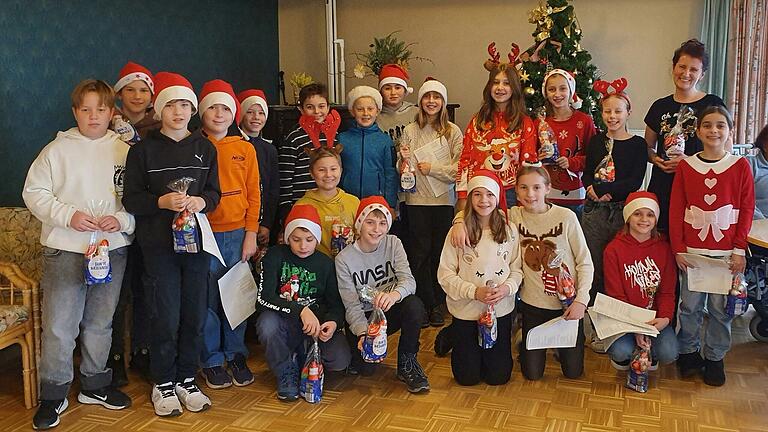 Englischlehrerin Lisa Bergmann zusammen mit den Schülerinnen und Schülern der Klasse 5c, die für ihre weihnachtlichen Gesangsdarbietungen ein süßes Dankeschön von der Seniorenresidenz Wiesentheid erhalten haben. Englischlehrerin Lisa Bergmann zusammen mit den Schülerinnen und Schülern der Klasse 5c, die für ihre weihnachtlichen Gesangsdarbietungen ein süßes Dankeschön von der Seniorenresidenz Wiesentheid erhalten haben.